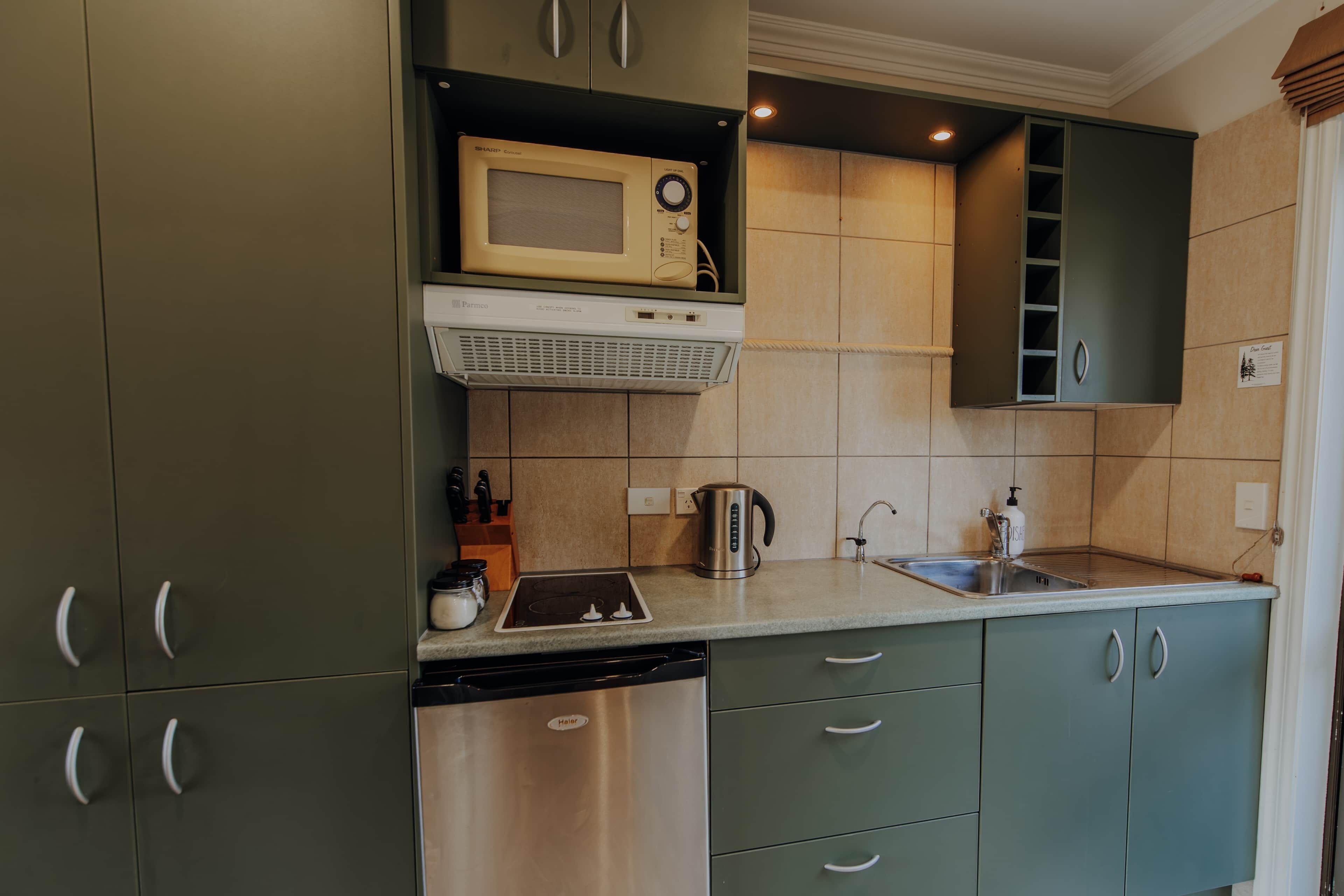 A kitchen with green cabinets, a microwave, a dishwasher, and a sink.