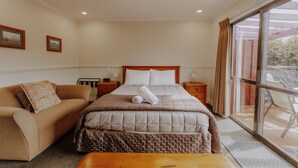 Une chambre d’hôtel avec un lit, un canapé, une table de chevet en bois et une fenêtre avec des rideaux.