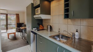 Une cuisine moderne dotée d’un four à micro-ondes encastré, d’un évier en acier inoxydable et de meubles de rangement verts.