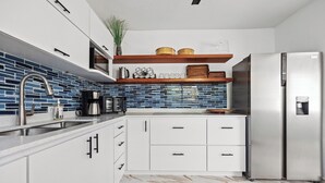 Una cocina moderna con armarios blancos, un refrigerador de acero inoxidable y un salpicadero de azulejos azules.