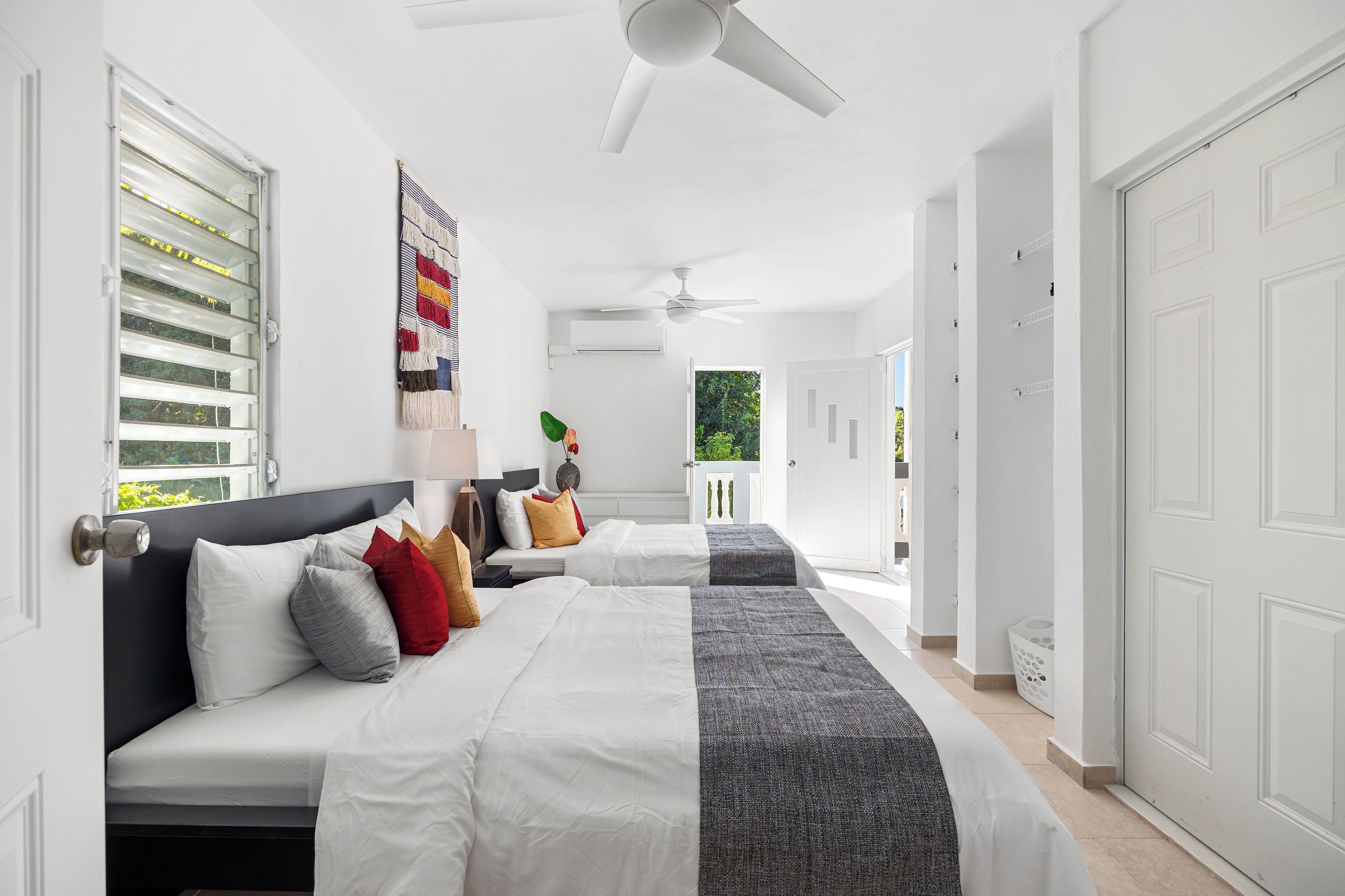 A bedroom with two beds, a ceiling fan, and a view of the outdoors.