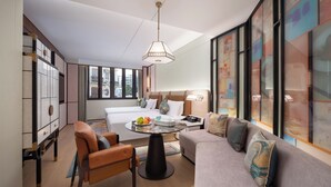 A modern hotel room with a bed, a sofa, a dining table, and a chair. There is a large window providing a view of the city. - Shantou DIOTEL Queen Hotel (Shantou)