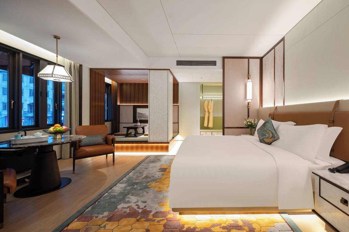 Una habitación de hotel moderna con una cama grande, un comedor y vistas a la ciudad.