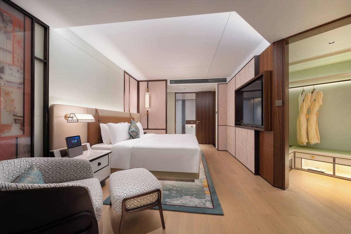 Una habitación de hotel moderna con una cama grande, un escritorio con una computadora portátil, un televisor y un vestidor con batas.