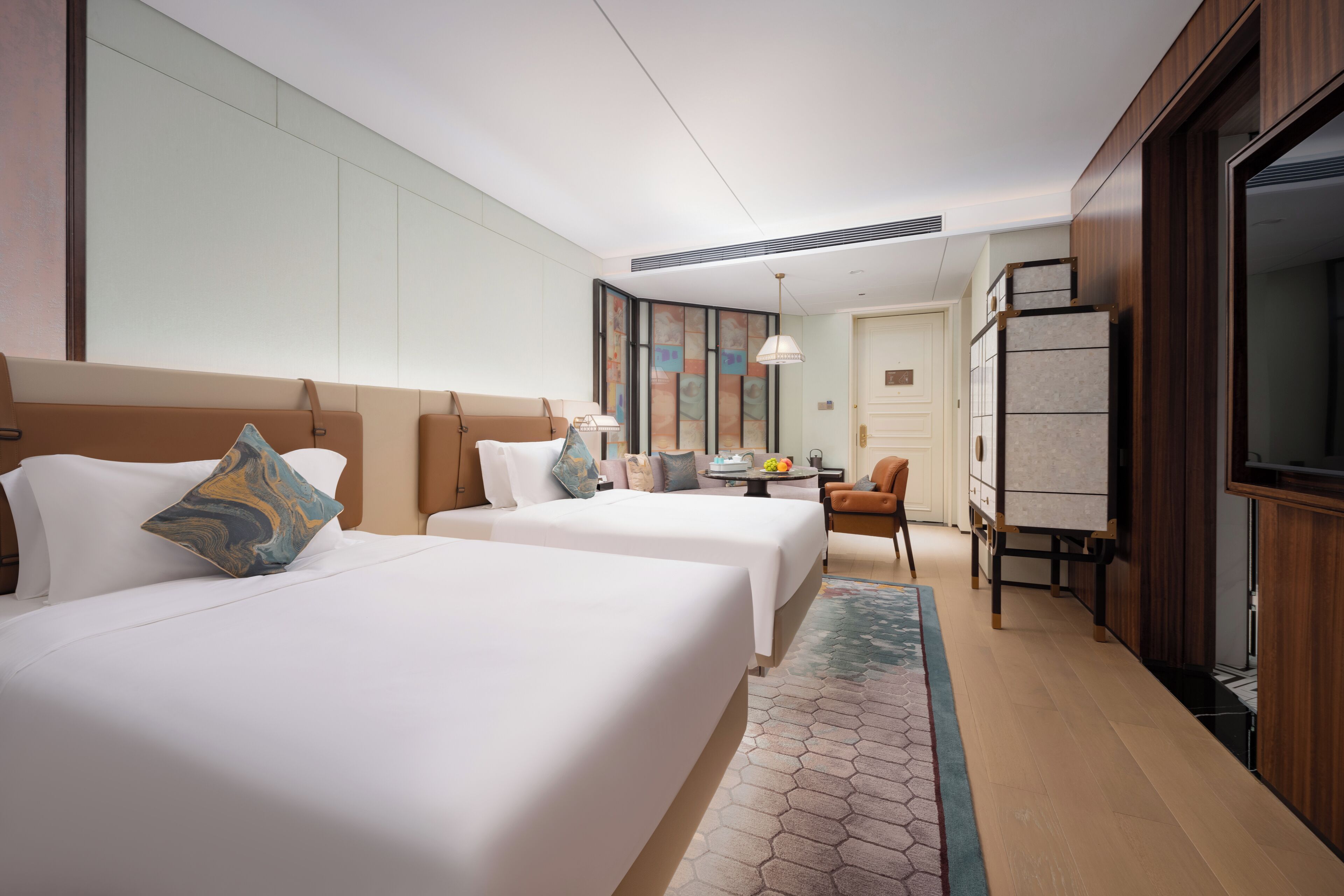 A hotel room with two beds, a desk, a chair, a TV, and a large window.