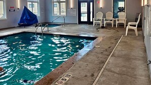 An indoor swimming pool with clear water, a diving board, and a covered area.