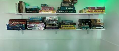 A room with a white wall and a shelf filled with various board games.