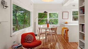 Une pièce lumineuse comprenant une table à manger, des chaises, un fauteuil rouge et une bibliothèque.