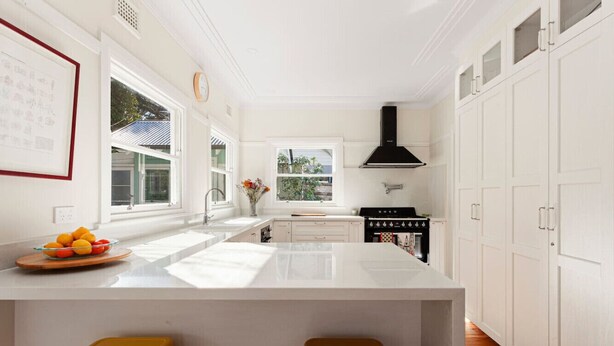 Une cuisine moderne dotée d’un grand îlot central, de meubles blancs et d’une hotte noire.