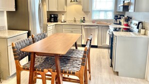 Een moderne keuken met witte kasten, roestvrijstalen apparatuur, een houten eettafel en een inbouwoven.