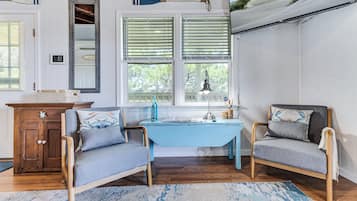 A room with a wooden desk, two chairs, a small table, and a window with blinds.