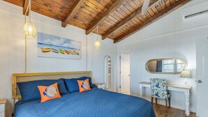 Ein Schlafzimmer mit einem großen Bett, Holzbalkendecke, einem Schreibtisch mit Stuhl und einem Gemälde von Booten an der Wand.