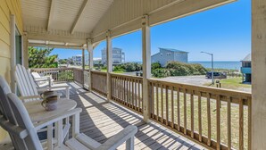 Eine überdachte Veranda mit weißen Stühlen und einem Tisch mit Blick auf einen Strand und Gebäude.