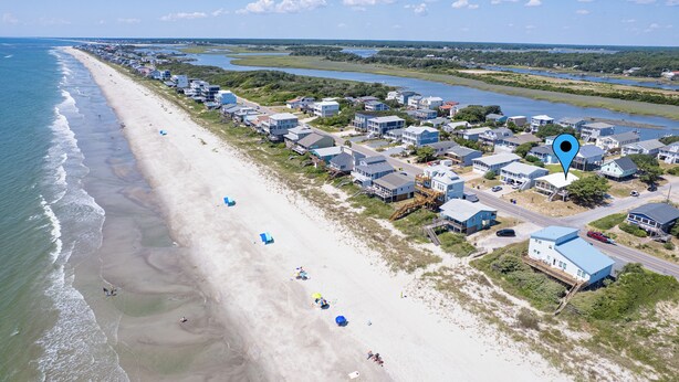 Luftaufnahme einer Küstenwohngegend mit Häusern direkt am Strand und einem Fluss.