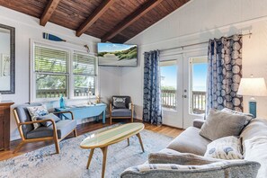 A cozy living room with a wooden ceiling, a television, a blue sofa, a small table, and a view of the outdoors through a window. - Oak Island Escape-2nd Row, Pet-Friendly w/ Ocean Views & Boat Ramp Nearby (Oak Island)
