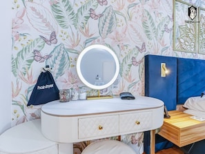 Un baño con tocador blanco, espejo redondo, cabecera azul y estampado de flores en la pared.