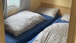 Interior compacto de una caravana con cama, almohadas y ventana que ofrece vistas al exterior.