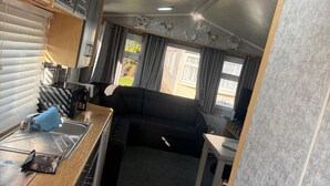 Interior compacto de autocaravana con kitchenette, sofá negro y pequeña mesa.