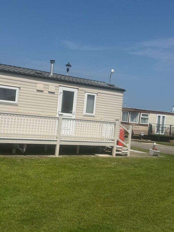 A mobile home with a fenced deck, a chimney, and a satellite dish.
