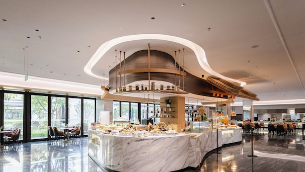 Un restaurante moderno con mostrador de mármol, amplias ventanas y un diseño de techo curvo.