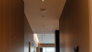 Un pasillo con puertas de madera, piso de baldosas y vista a una habitación con mesa y sillas.