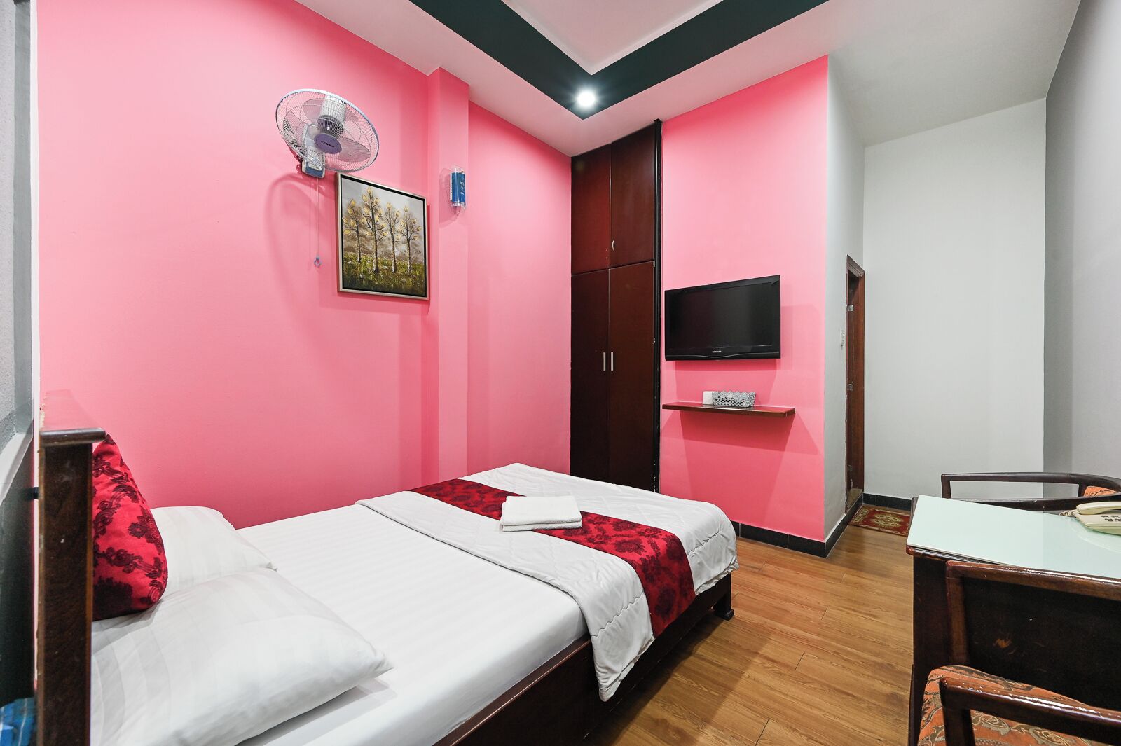 A room with two single beds, a desk, a chair, a TV, a wardrobe, and a fan.