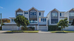 Een rij moderne twee-onder-een-kapwoningen met een wit hek, een heldere lucht en een verzorgd gazon.