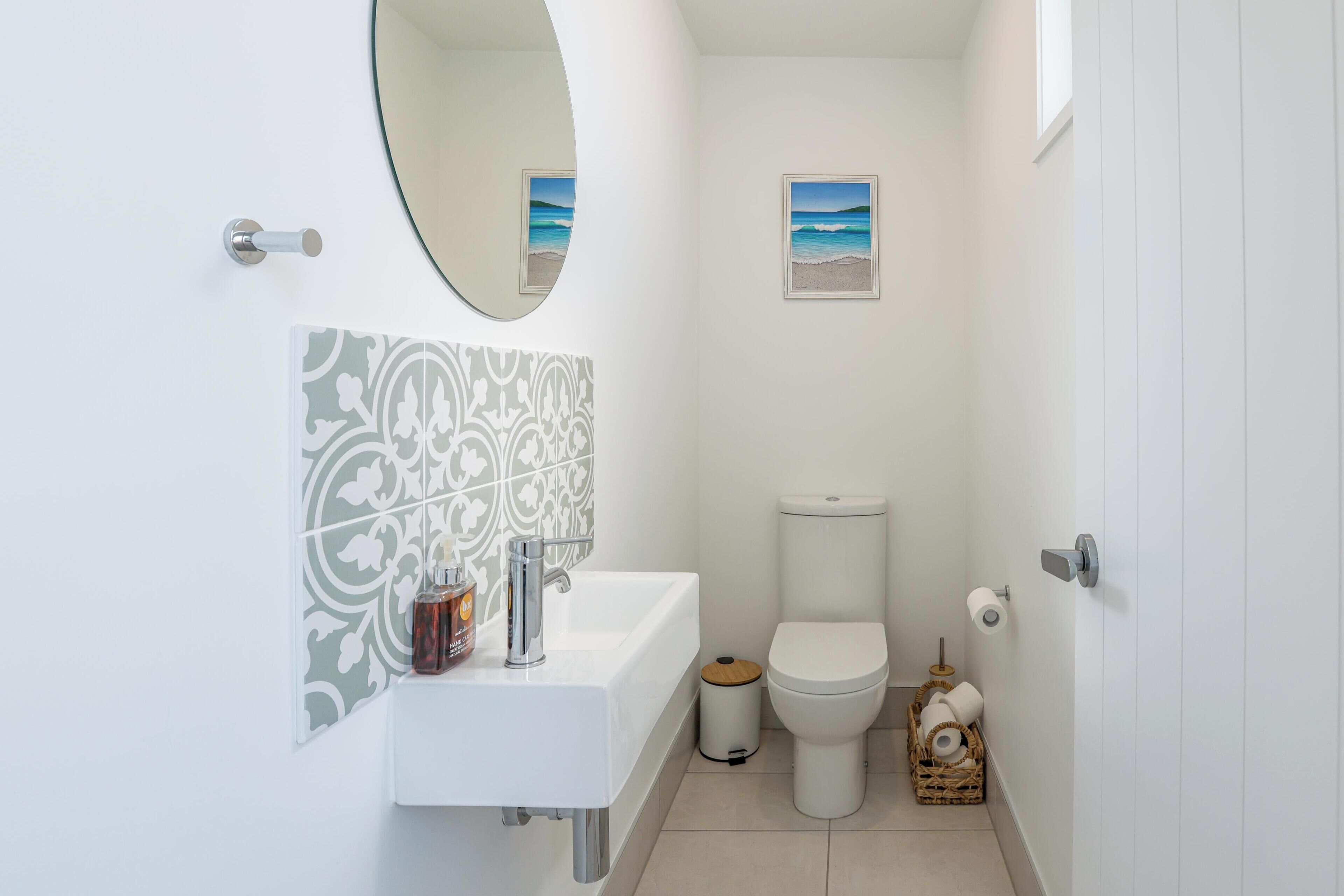 A compact bathroom with a white sink, a toilet, a small framed picture of a beach, and a mirror.
