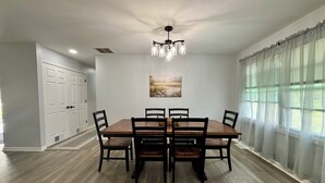 A dining room with a wooden table and chairs, a chandelier, and a painting on the wall.