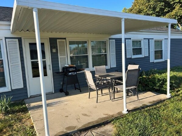 A covered patio area with a table and chairs, a grill, and a window with shutters.