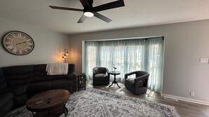 A living room with a ceiling fan, a clock, a sofa, a coffee table, and a patterned rug.