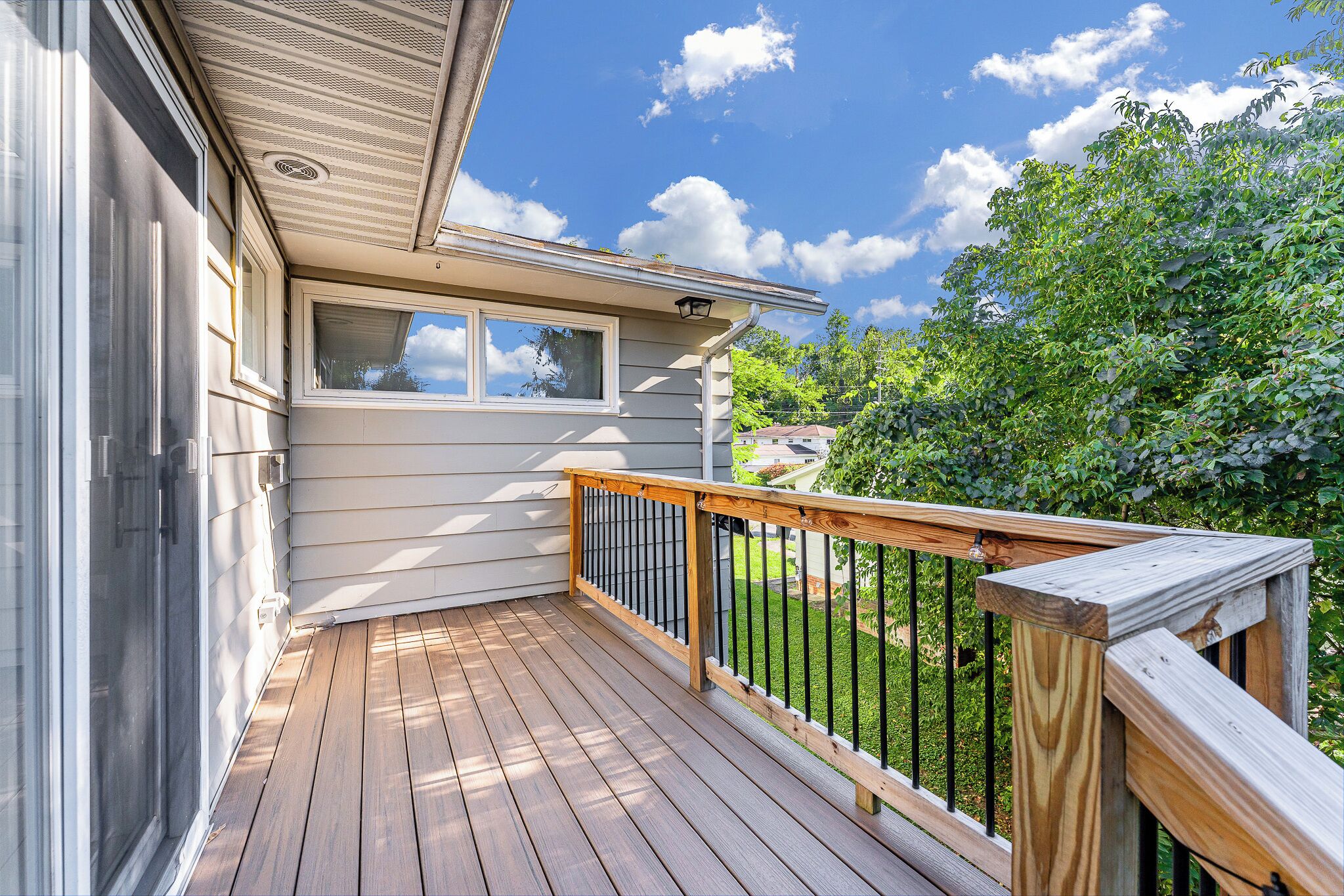 A wooden deck with a railing, a window, and a view of a green landscape.