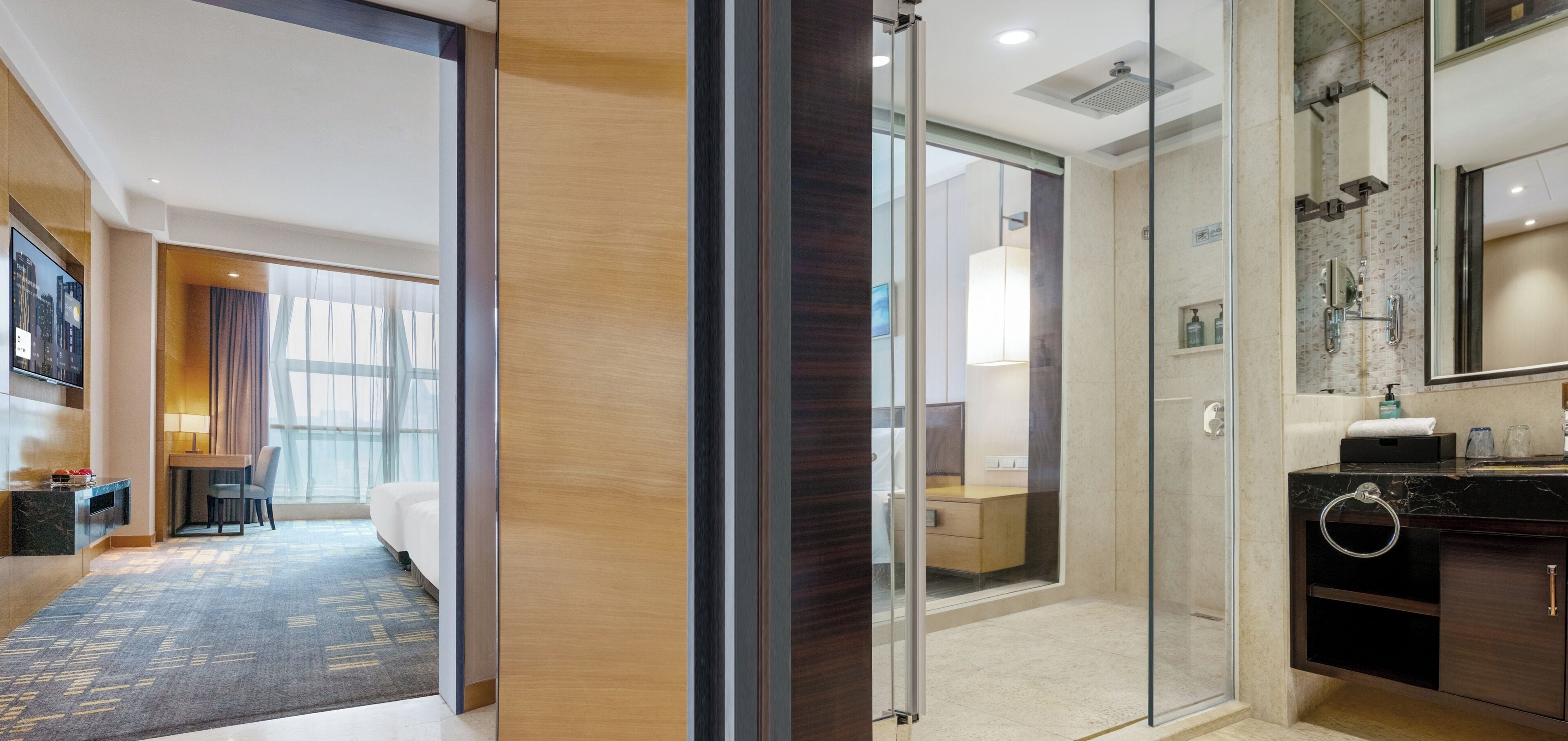 A hotel room with a glass-enclosed shower, a wooden floor, a desk with a chair, and a bed.