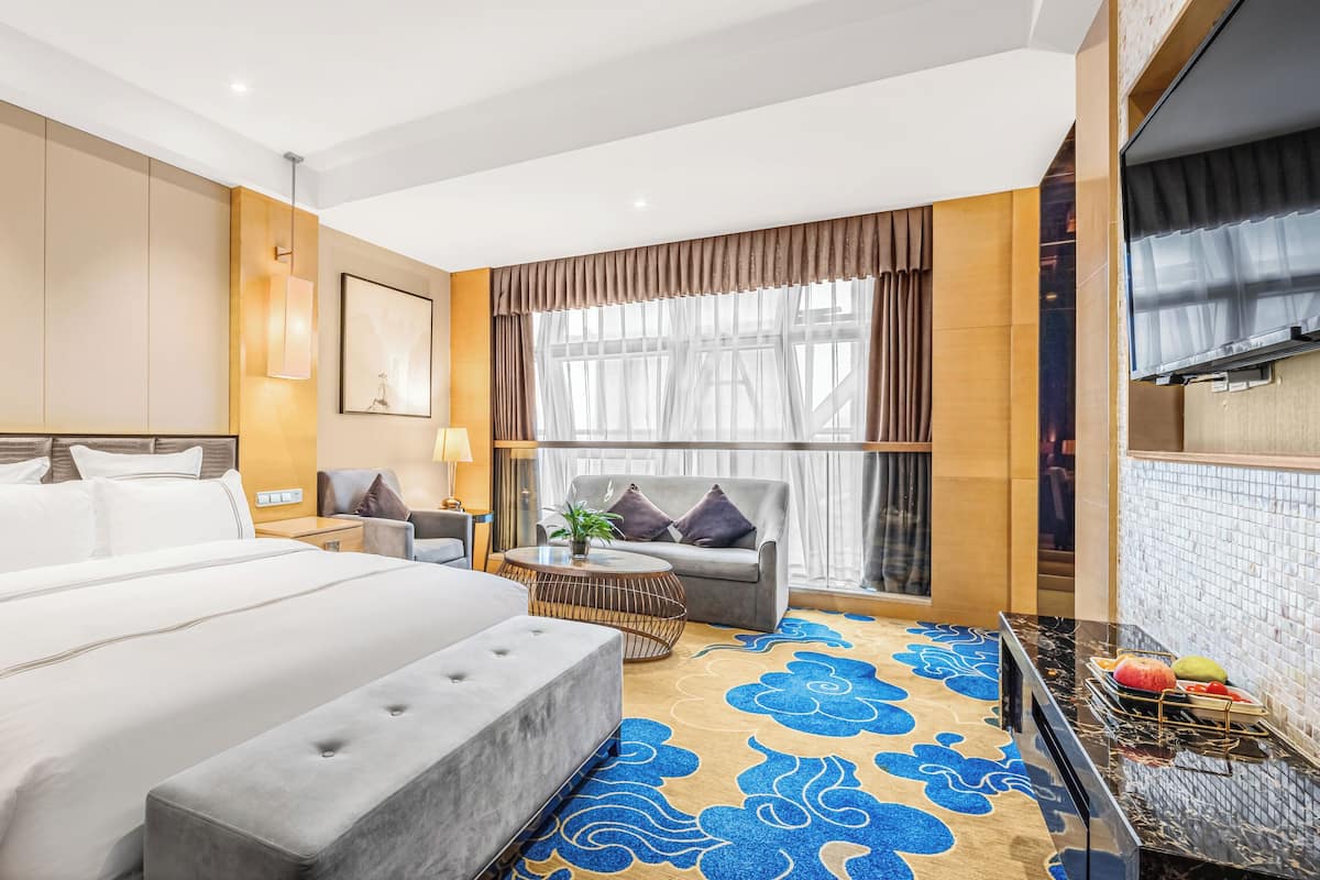 Habitación de hotel con cama, sofá, televisor, una mesita y una ventana con cortinas.