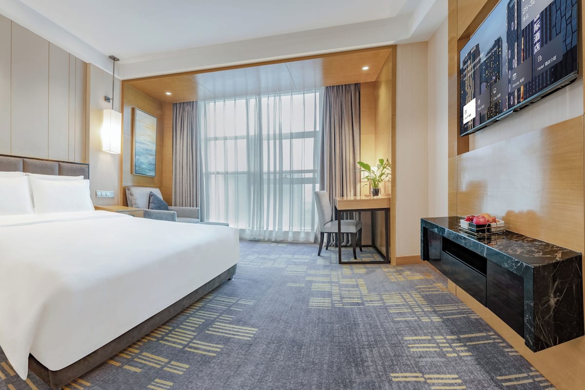 Habitación de hotel con una cama grande, un escritorio, una silla, un televisor y una ventana con cortinas.