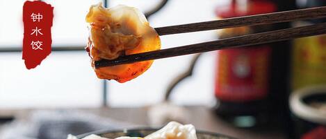 A bowl of dumplings with chopsticks lifting one.