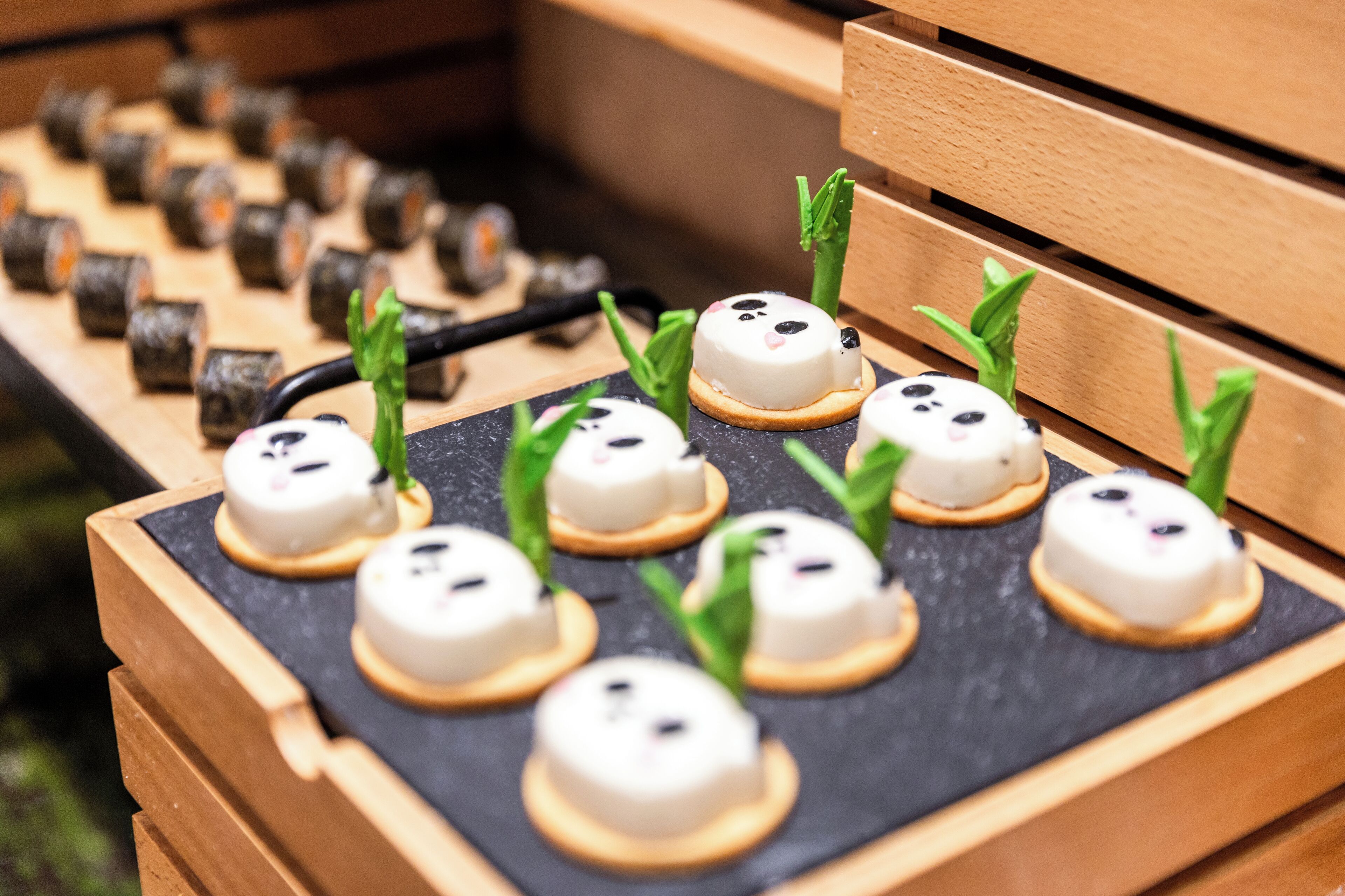 Una bandeja con sushi y pasteles pequeños, decorados con hojas verdes, sobre una losa negra.