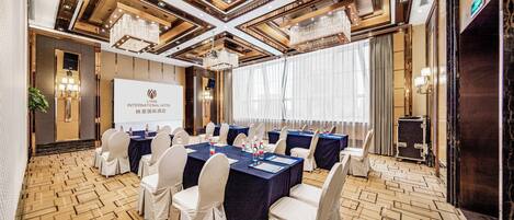 Un salón de conferencias con una pantalla grande, mesas, sillas y una araña.