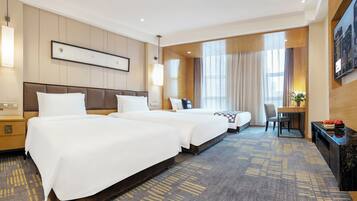 A hotel room with two beds, a desk, a chair, a TV, and a large window with curtains.