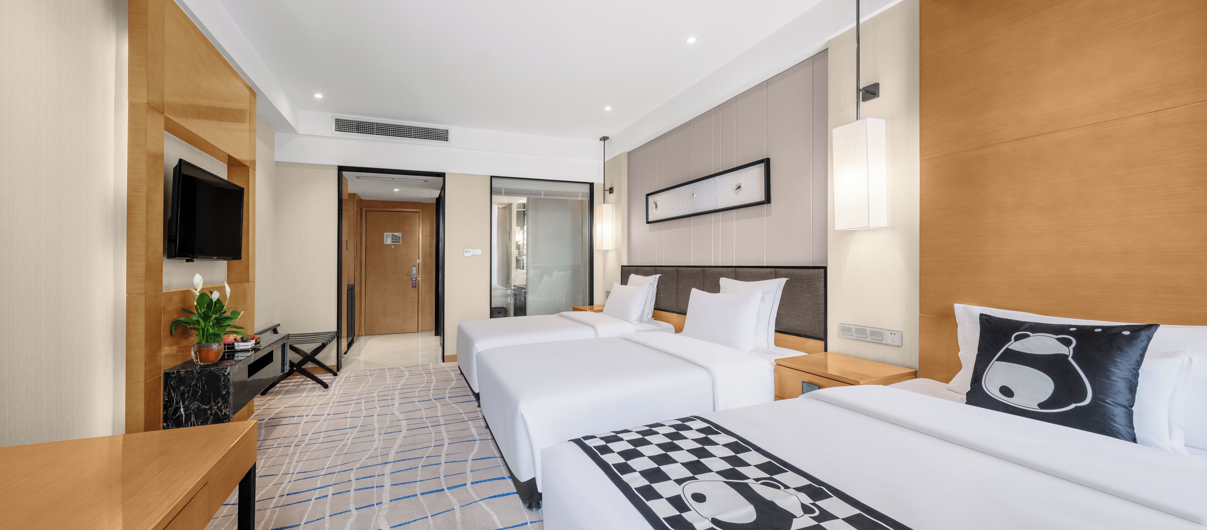 A hotel room with a large bed, a smaller bed, a desk, a TV, and a bathroom visible through a glass door.