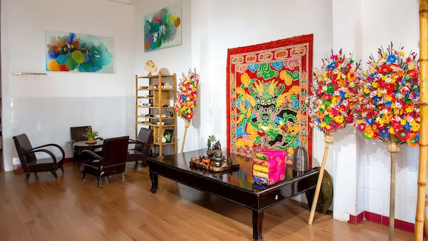 A room with a wooden floor, a black table with decorative items, a colorful tapestry, and a bookshelf. - Moc Truly Hue Homestay (Hue)