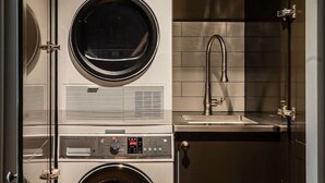 A compact laundry room with two stacked front-loading washing machines and a built-in sink. - Historic Castle Coach House – Trail & Wineries (Earnscleugh)