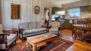 A living room with a sofa, chairs, a coffee table, and a dining area with a table and chairs. - Historic Castle Coach House – Trail & Wineries (Earnscleugh)