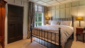 A bedroom with a bed, two bedside tables, a window with curtains, and a door. - Historic Castle Coach House – Trail & Wineries (Earnscleugh)
