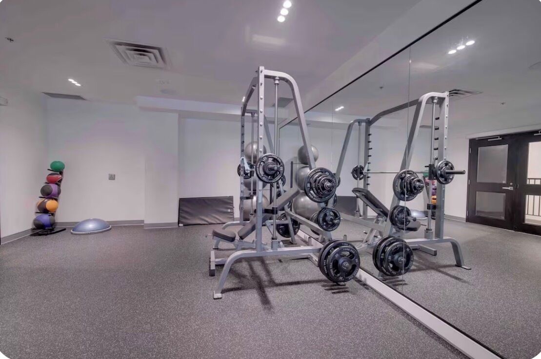Une salle de sport équipée de matériel de musculation, de ballons d’exercice et d’un miroir.