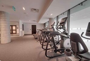 Une salle de sport avec des tapis de course alignés le long d’un mur, d’un pilier et d’une porte donnant sur une autre pièce.