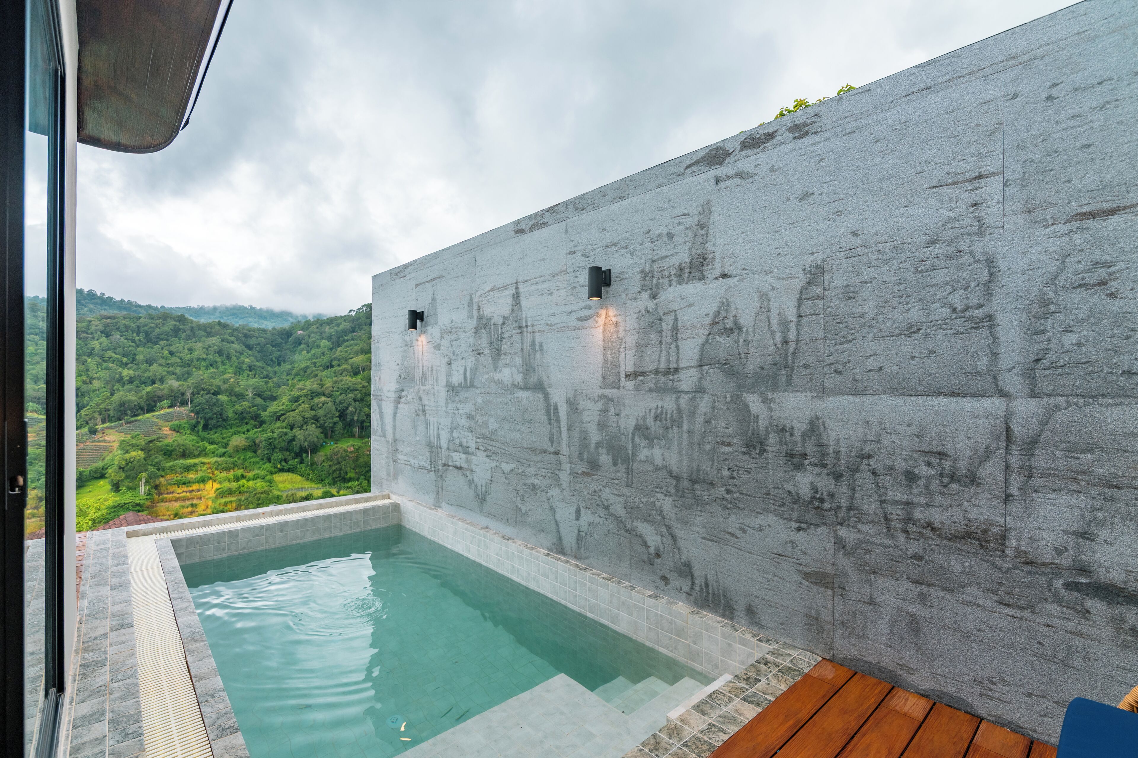 A modern outdoor pool with a stone wall and a view of a lush landscape.