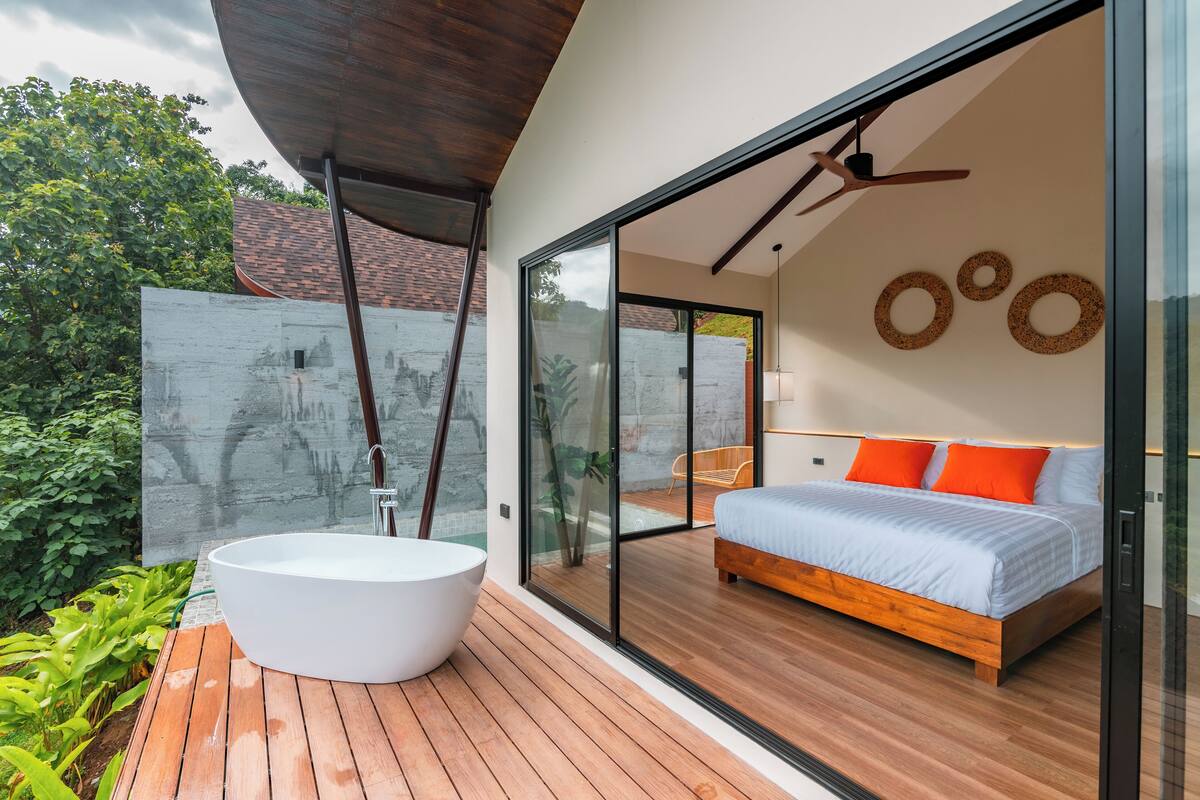 A modern bedroom with a large bed, a white bathtub, and a glass door leading to a balcony.