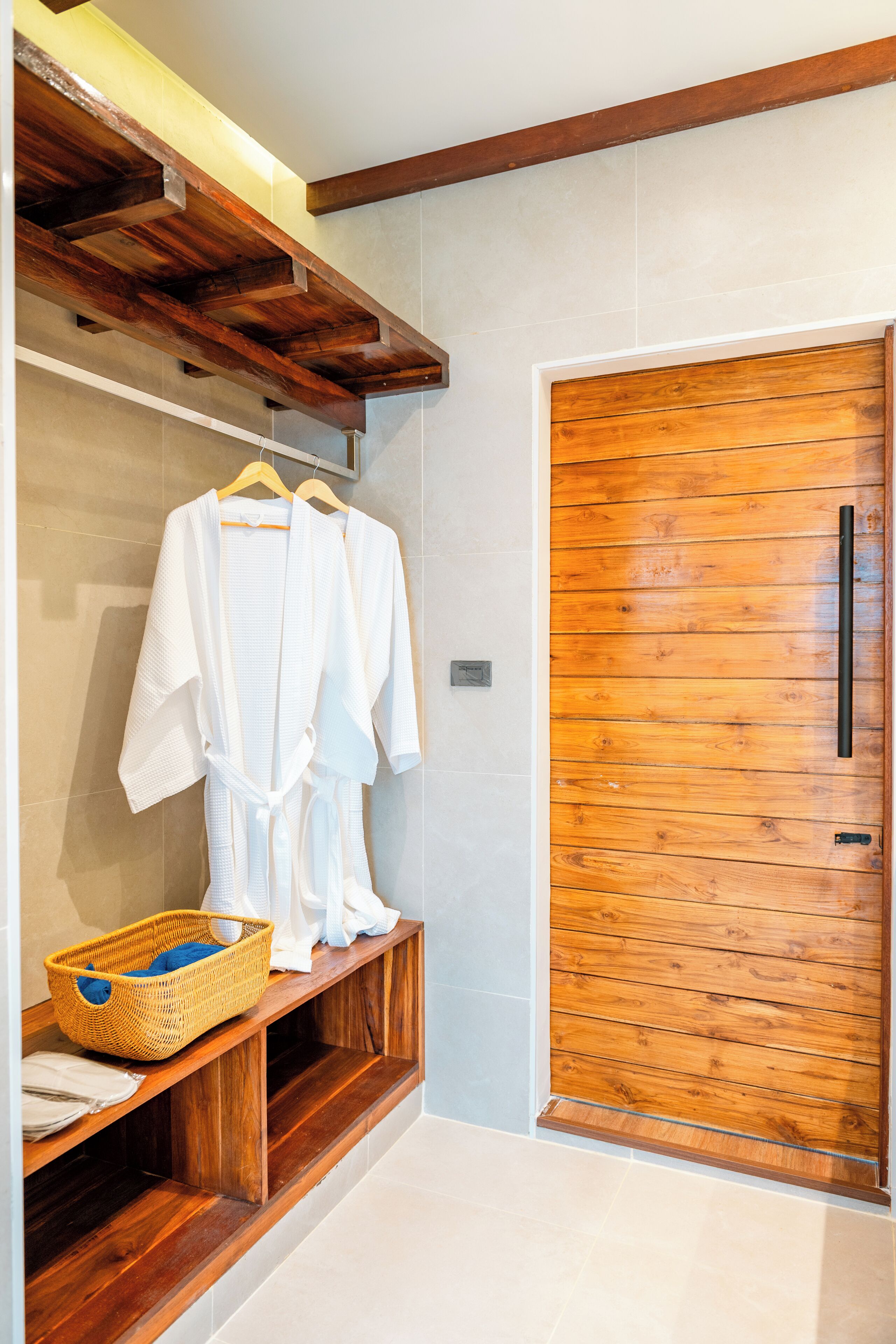 Un baño con estantes de madera, una puerta de madera y una bata blanca colgada en un perchero.