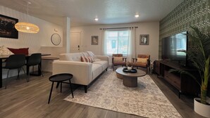 A modern living room with a sofa, chairs, a coffee table, a TV, and a large window with curtains.